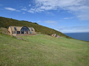 A single-story building with a curved roof, a covered patio, and a view of the sea.