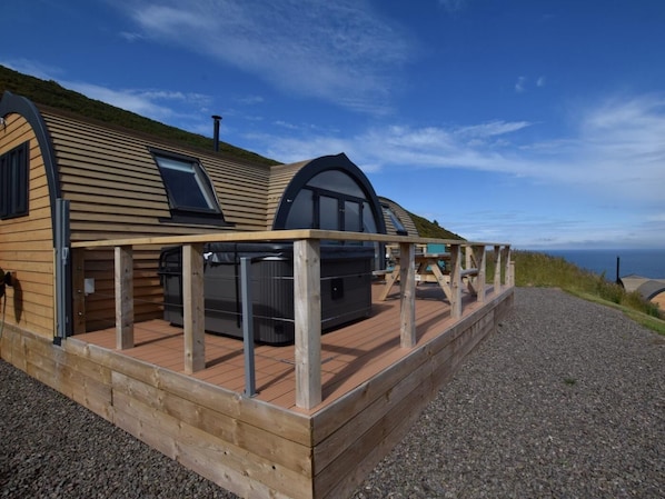 A wooden cabin with a deck, a hot tub, and a view of the sea.