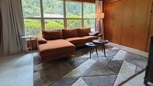 A room with a sofa, a small table, a lamp, and a view of greenery outside. - Touchdown on Terrace - Gator Retreat 1 mile to UF - Sleeps 6. (Gainesville)