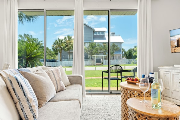 A living room with a sofa, a table with a bottle and glasses, and a view through large windows.