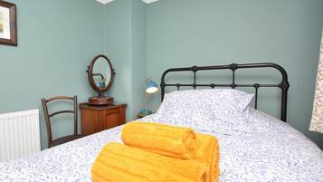A bedroom with a bed, a nightstand, a chair, a radiator, and a mirror.