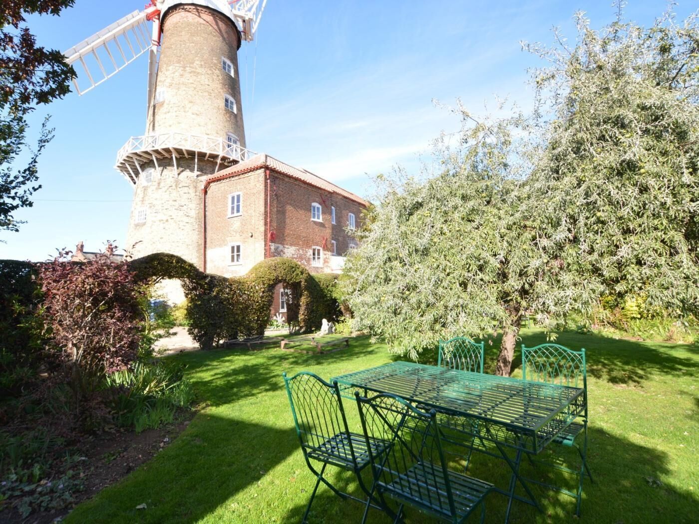A windmill, a brick building, and a green metal table with chairs in a garden.