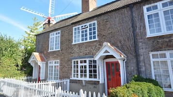A traditional brick house with white window frames, a red door, and a white picket fence.