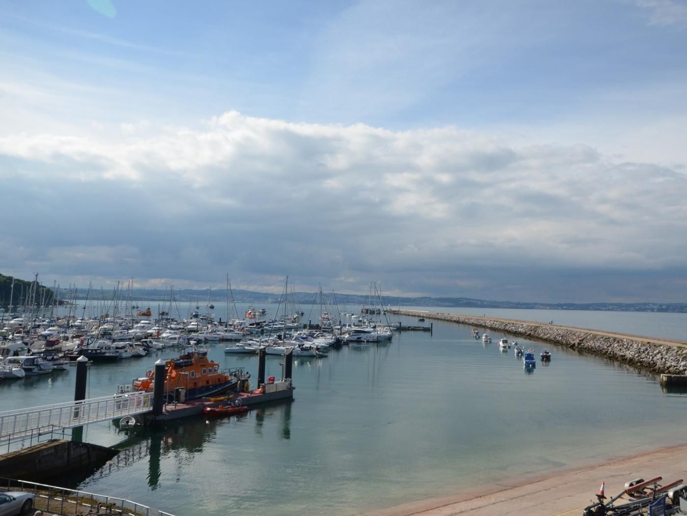 A marina with boats docked, a bridge, and a calm sea under a cloudy sky.