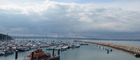A marina with boats docked, a bridge, and a calm sea under a cloudy sky.
