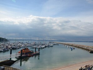 Un port de plaisance avec des bateaux amarrés, un pont et une mer calme sous un ciel nuageux.