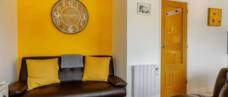 Una habitación con un sofá de cuero marrón, una puerta de madera, un radiador y un reloj en la pared.