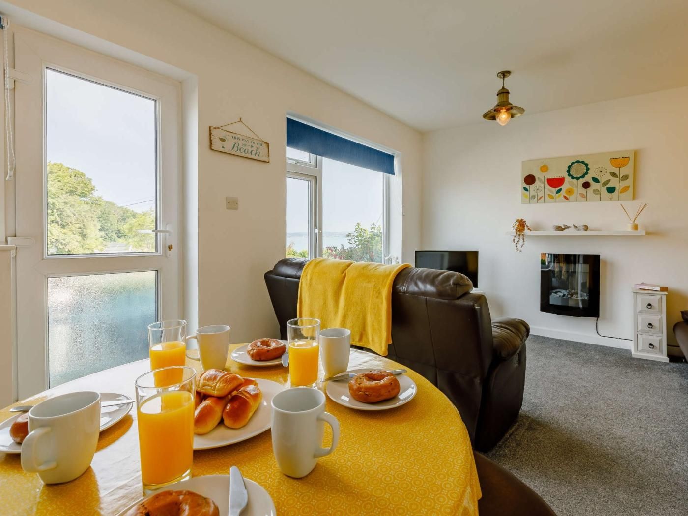 A room with a dining table set for breakfast, a leather sofa, a TV, and a fireplace.