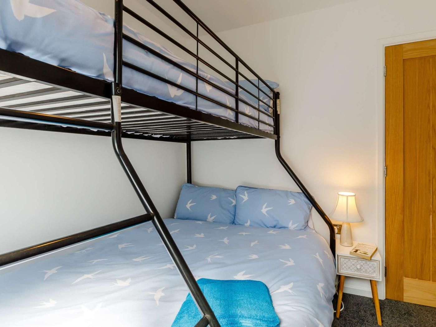 Un lit superposé avec une tête de lit, une table de chevet avec une lampe et une porte en bois.