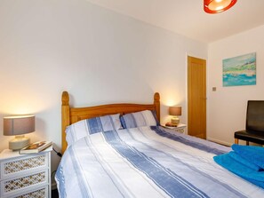 A bedroom with a wooden bed, two bedside tables with lamps, a door, and a painting on the wall. - 2 Bed in Brixham (oc-88998) (Brixham)