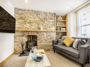 Ein Wohnzimmer mit Steinwand, Kamin, grauem Sofa mit Kissen, Couchtisch mit Schale und Gläsern sowie Bücherregal.