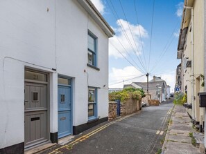 A narrow street with buildings on either side, a clear sky, and a visible power line. - 2 Bed in Brixham (oc-89055) (Brixham)