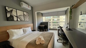 Una camera d'albergo con un letto, una scrivania, una sedia, un balcone e vista sugli edifici.