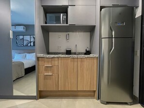 A compact kitchen with a stainless steel refrigerator, a microwave, and wooden cabinets. - On Jurupis - Livinn by Travel Inn OJ2 (São Paulo)