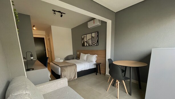 Una camera d'albergo moderna con un letto, un tavolino rotondo, un divano e un angolo cottura.