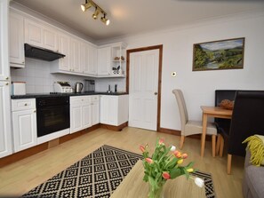 A modern kitchen with white cabinetry, a black oven, and a dining area with a wooden table and chairs. - 1 Bed in Saundersfoot (oc-fb246) (Saundersfoot)
