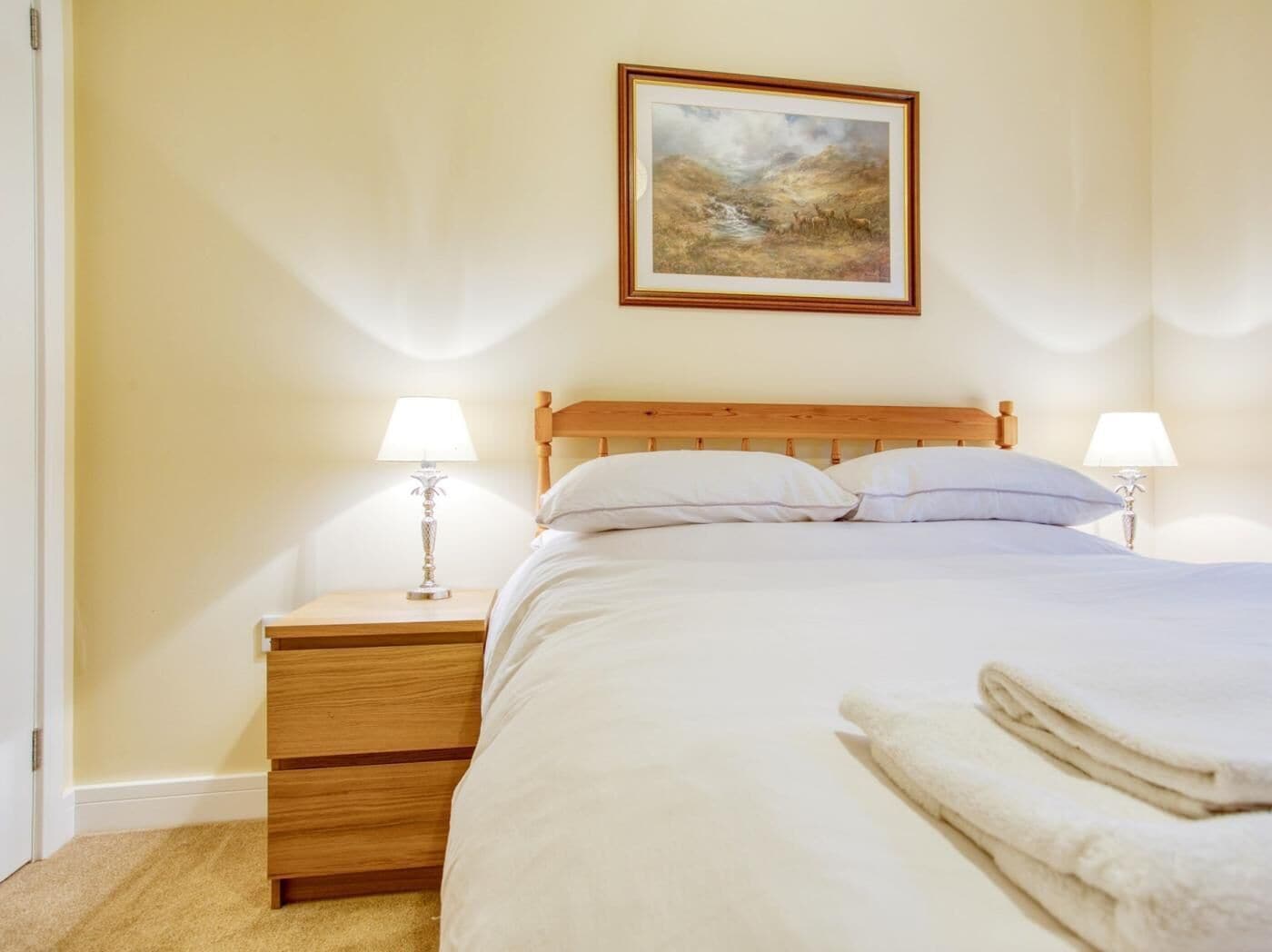 Una cama bien hecha con sábanas blancas, cabecera de madera y dos lámparas de noche.