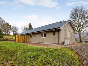 Ein eingeschossiges Gebäude mit geneigtem Dach, einem eingezäunten Garten und blauem Himmel.