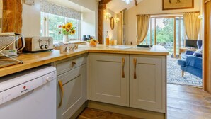 A kitchen with a central island, a built-in dishwasher, and a dining area with a blue sofa. - 3 Bed in Brecon (oc-bn065) (Crai)