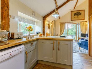 A kitchen with a central island, a built-in dishwasher, and a dining area with a blue sofa. - 3 Bed in Brecon (oc-bn065) (Crai)