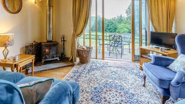 A cozy living room with a fireplace, a sofa, a television, and a view of the outdoors. - 3 Bed in Brecon (oc-bn065) (Crai)