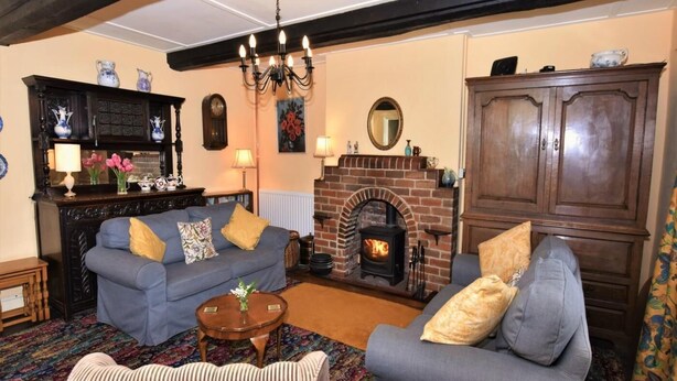 Ein gemütliches Wohnzimmer mit Kamin, zwei Sofas, einem gemusterten Teppich und einer Holzkommode.