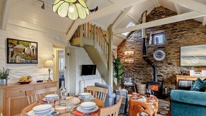 Ein gemütliches Wohnzimmer mit Steinwand, Kamin, Essbereich mit Holzmöbeln und einer Treppe.