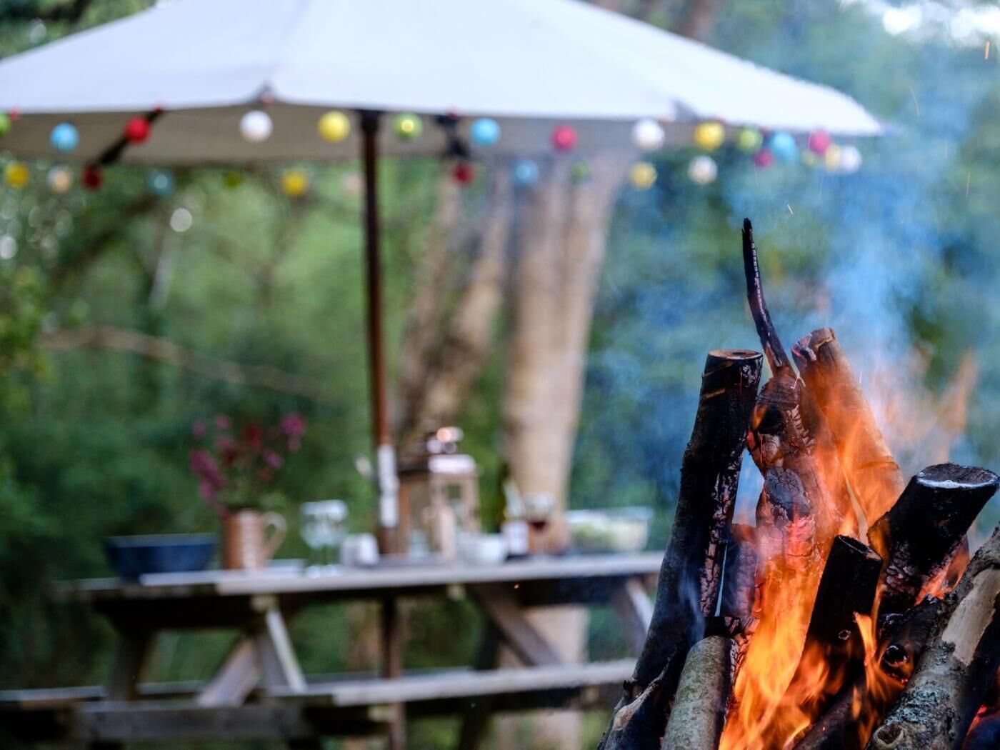 A campfire with a table and umbrella in the background.