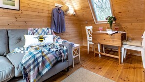 Een gezellig vakantiehuisje met een bank, een eettafel en een raam met uitzicht op bomen.