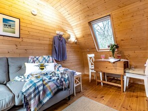 Ein gemütliches Blockhaus mit einer Couch, einem Esstisch und einem Fenster mit Blick auf Bäume.