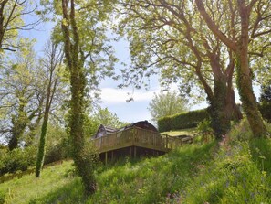 A wooden cabin with a deck, surrounded by lush greenery and flowering plants.