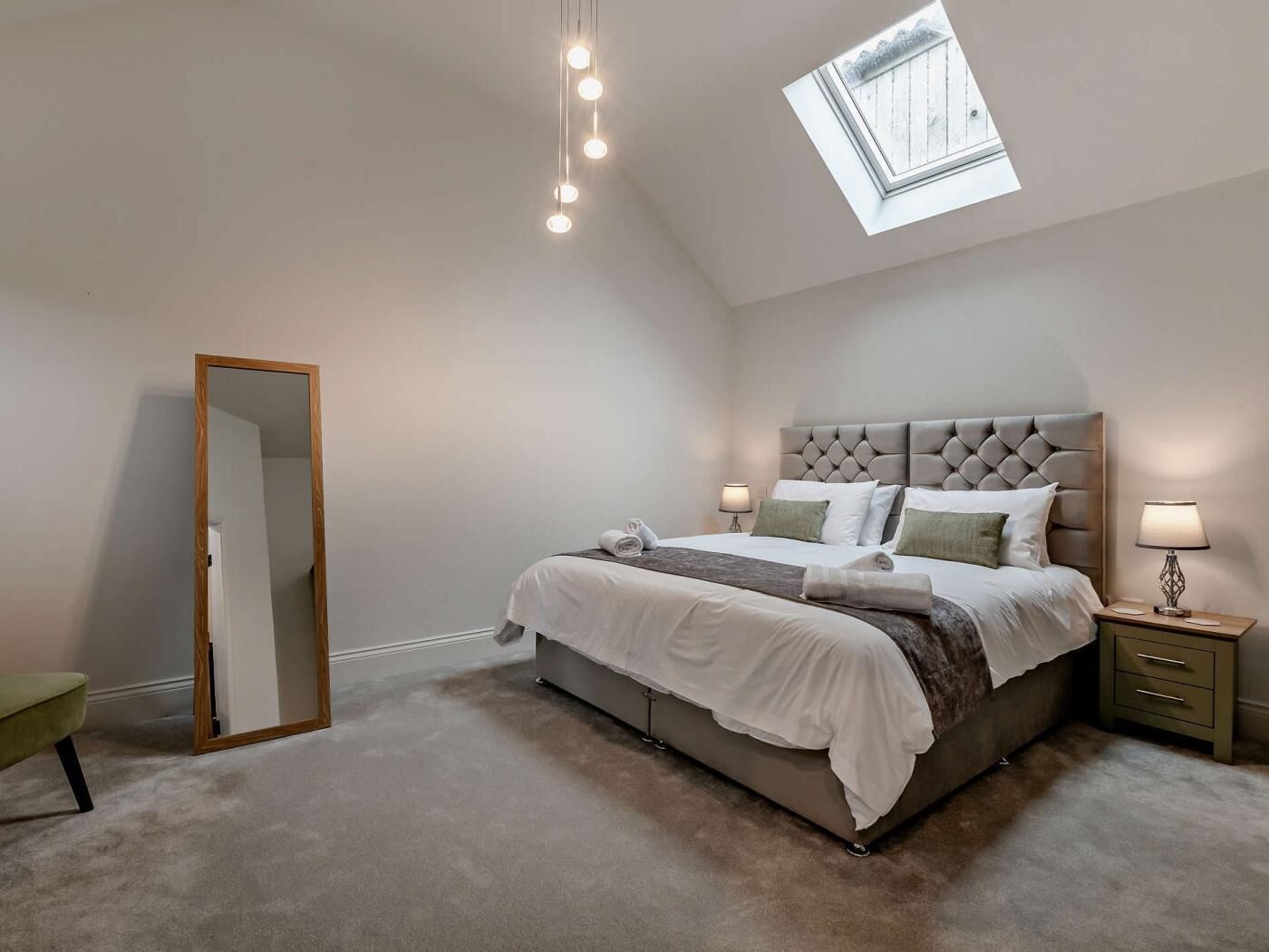 A bedroom with a bed, bedside lamps, a mirror, and a skylight.