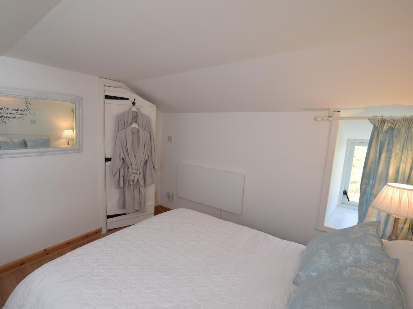 Een slaapkamer met een groot bed, een kledingkast, een spiegel en een raam met gordijnen.