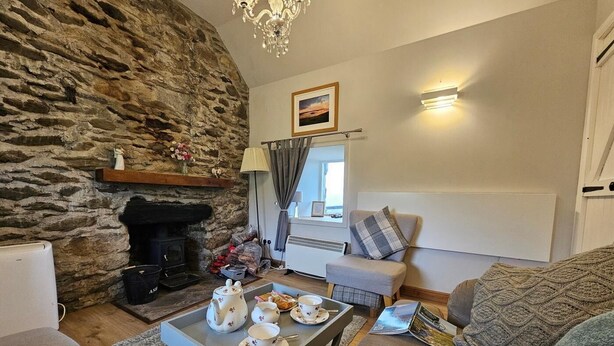 A cozy living room with a stone wall, a fireplace, a sofa, a coffee table with tea set, and a window with curtains.
