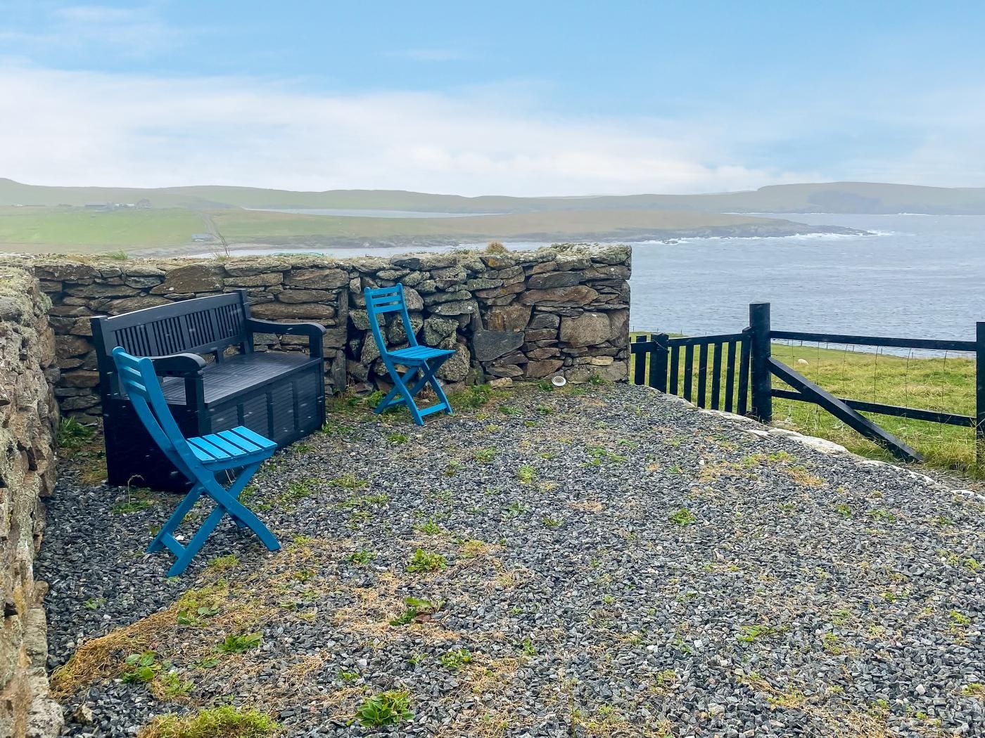 A stone wall with a bench and a chair, overlooking a body of water.