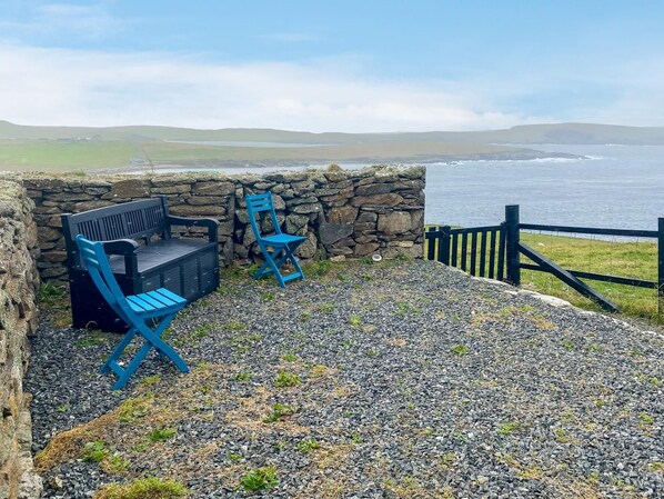 A stone wall with a bench and a chair, overlooking a body of water.