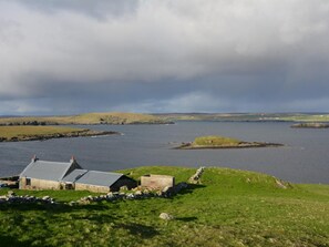 A coastal landscape with a house and a small island in the distance. - 1 Bed in Shetland (oc-75417) (Uyeasound)
