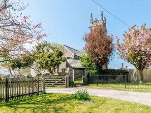 A stone building with a tower, surrounded by a wooden fence and flowering trees. - 1 Bed in Bideford (oc-51784) (Fairy Cross)