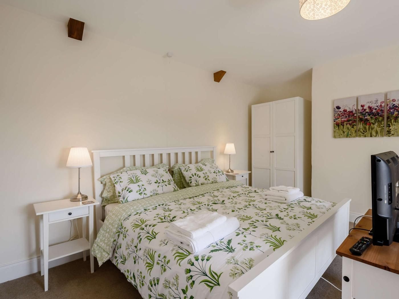 Une chambre à coucher avec un lit, deux tables de chevet, une armoire, un tableau et un téléviseur.