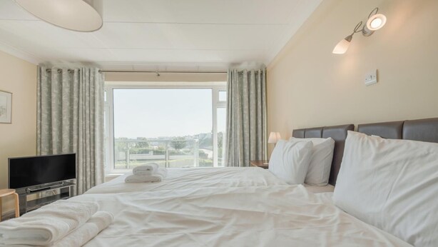 Ein Hotelzimmer mit einem großen Bett, einem Flachbildfernseher, einem Nachttisch und Blick ins Freie.