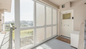 Ein Balkon mit großen Fenstern, eine Tür mit Nummernschild und eine Betontreppe.