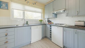 Eine Küche mit hellblauen Schränken, einem Fenster, einem Gasherd und einem Geschirrgestell.