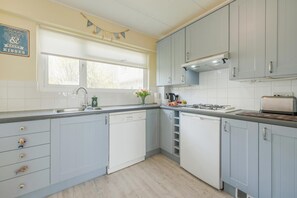 A kitchen with light blue cabinets, a window, a gas stove, and a dish rack. - 2 Bed in Tenby (oc-fb065) (Tenby)