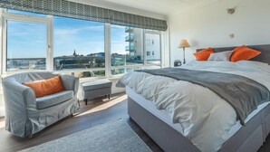 Een slaapkamer met een groot bed, een stoel, een tafel en uitzicht op een stadsgezicht.