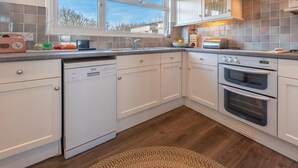Een moderne keuken met witte kasten, een vaatwasser, een dubbele oven en een raam met uitzicht op bomen.