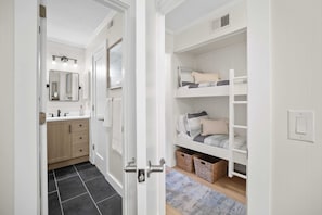 Ein Zimmer mit Etagenbett, ein Badezimmer mit Spiegel und Waschbecken sowie eine Tür zu einem weiteren Raum.