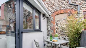Eine moderne Küche mit Glastür, Steinwand und kleiner Sitzecke im Freien mit Tisch und Stühlen.