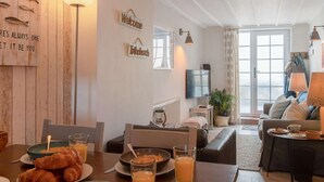 Ein gemütliches Wohnzimmer mit einer Couch, einem Couchtisch und einem Essbereich, der für das Frühstück gedeckt ist.