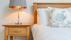 Una cama con almohadones estampados, una lámpara de noche y una mesita de madera con un cajón.