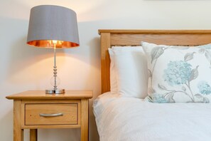 Ein Bett mit blumigen Kissen, eine Nachttischlampe und ein Nachttisch aus Holz mit einer Schublade.
